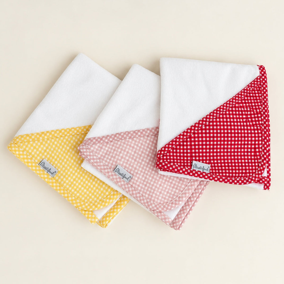 Três fraldas de pano brancas para bebé com acabamento em padrão vichy amarelo, rosa seco e vermelho.