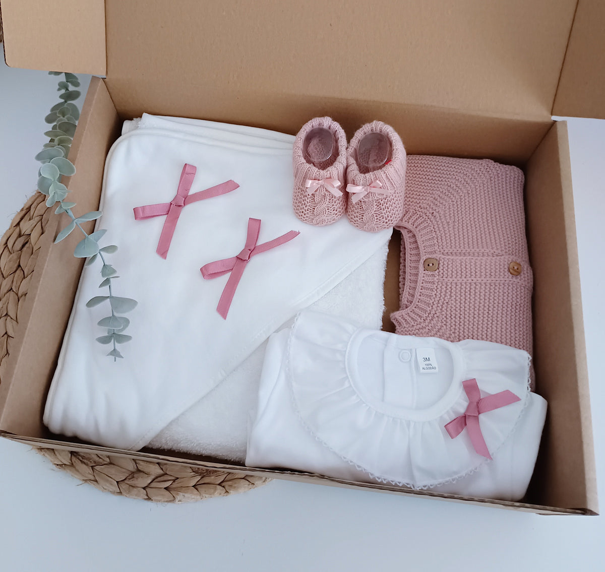 Pack de nascimento para bebé em branco e rosa velho, composto por toalha de banho com laços, body de gola, casaco de malha e carapins com laços.