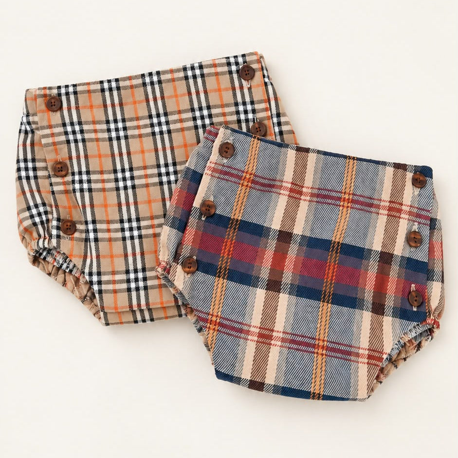 Dois tapa-fraldas para bebé com estampado xadrez e botões castanhos nas laterais, um em bege com preto e laranja e outro em azul, bege e vermelho.