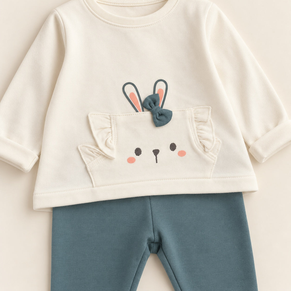 Conjunto de bebé com camisola pérola de manga comprida, bolso decorado com cara de coelho, orelhas e laço verde, combinado com leggings verde-escuro.