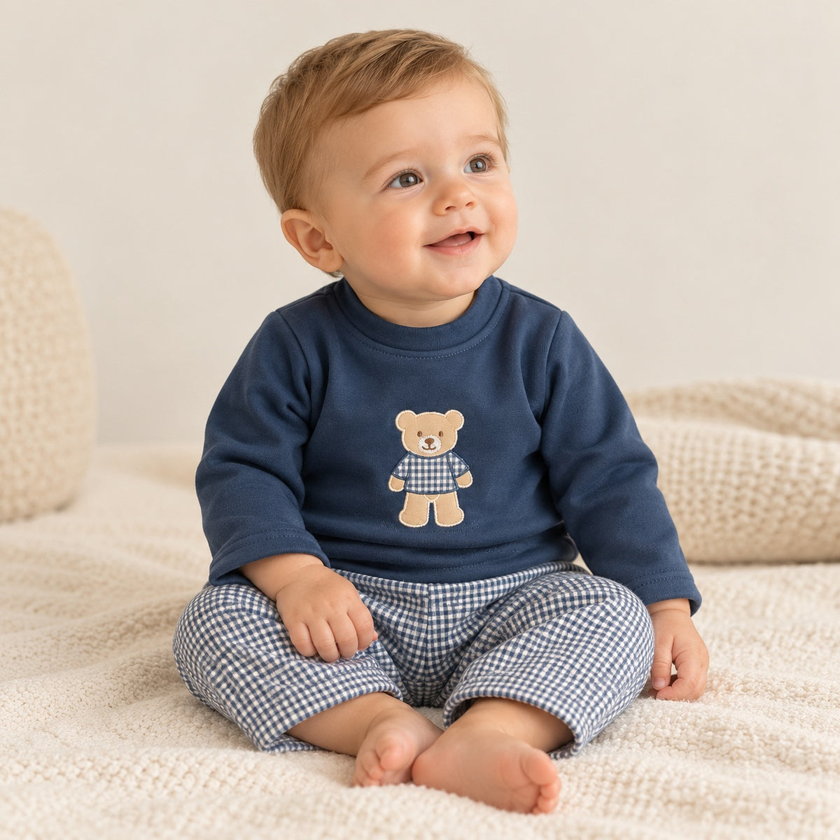Conjunto de bebé com camisola azul-marinho de manga comprida e aplicação de urso, combinado com calças forradas de padrão vichy azul e branco.