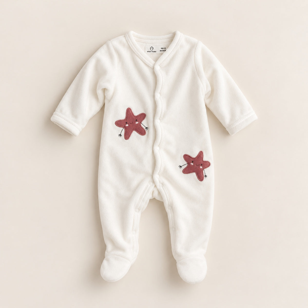 Babygrow de veludo pérola para bebé, com mangas compridas, pés fechados, abertura frontal com molas e duas aplicações de estrelas rosa.