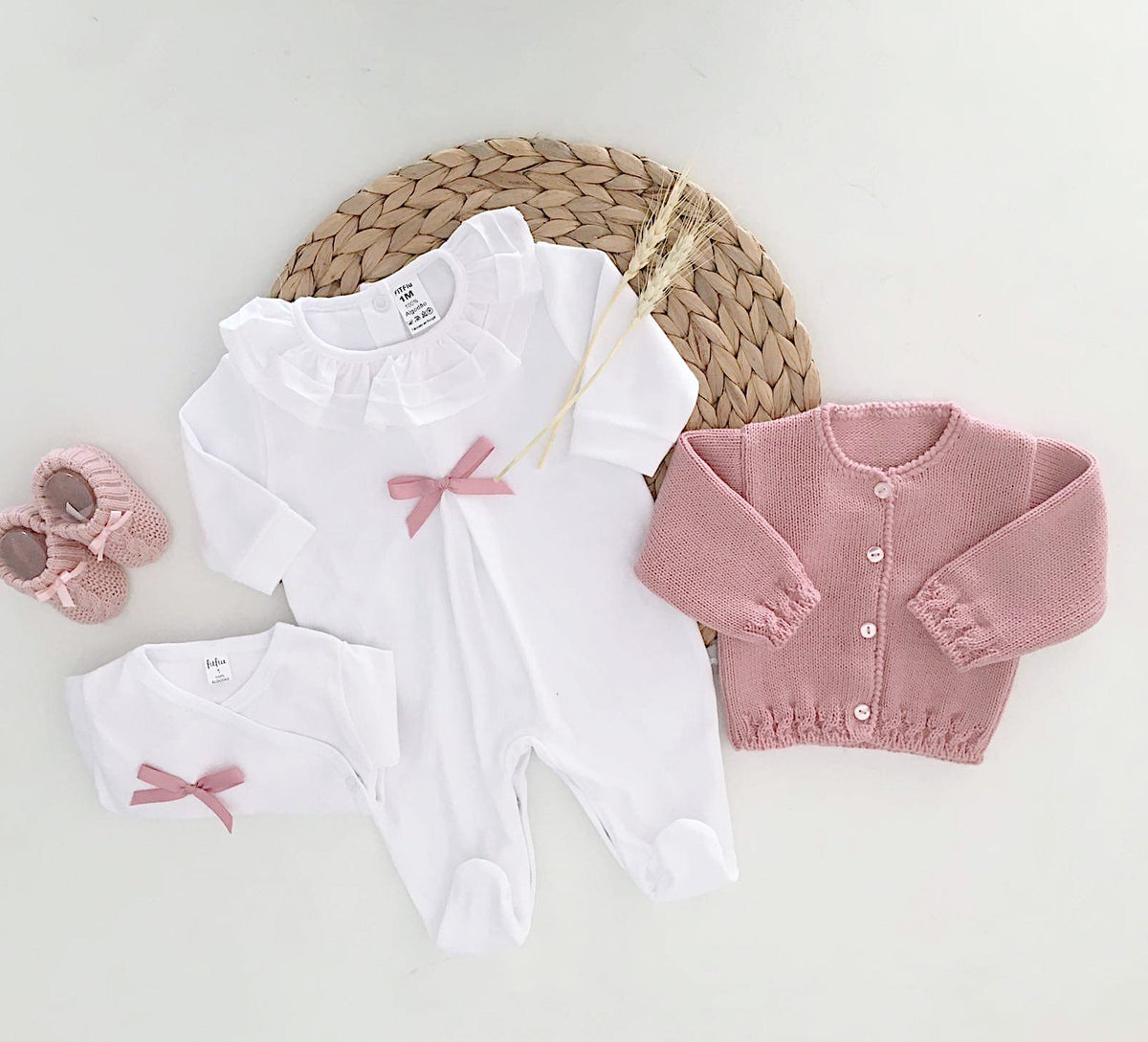 Conjunto primeira roupinha de bebé com babygrow branco de gola com folho e laço rosa velho, body a condizer, calças com pé, casaco de malha e carapins rosa velho.
