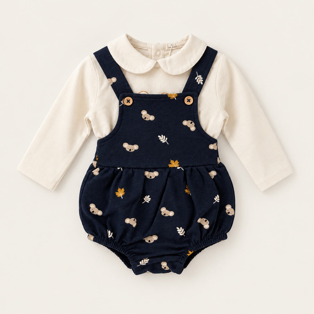 Fofo azul-marinho para bebé com estampado de koalas e folhas, alças com botões de madeira e corte franzido, combinado com camisola pérola de manga comprida e gola arredondada.