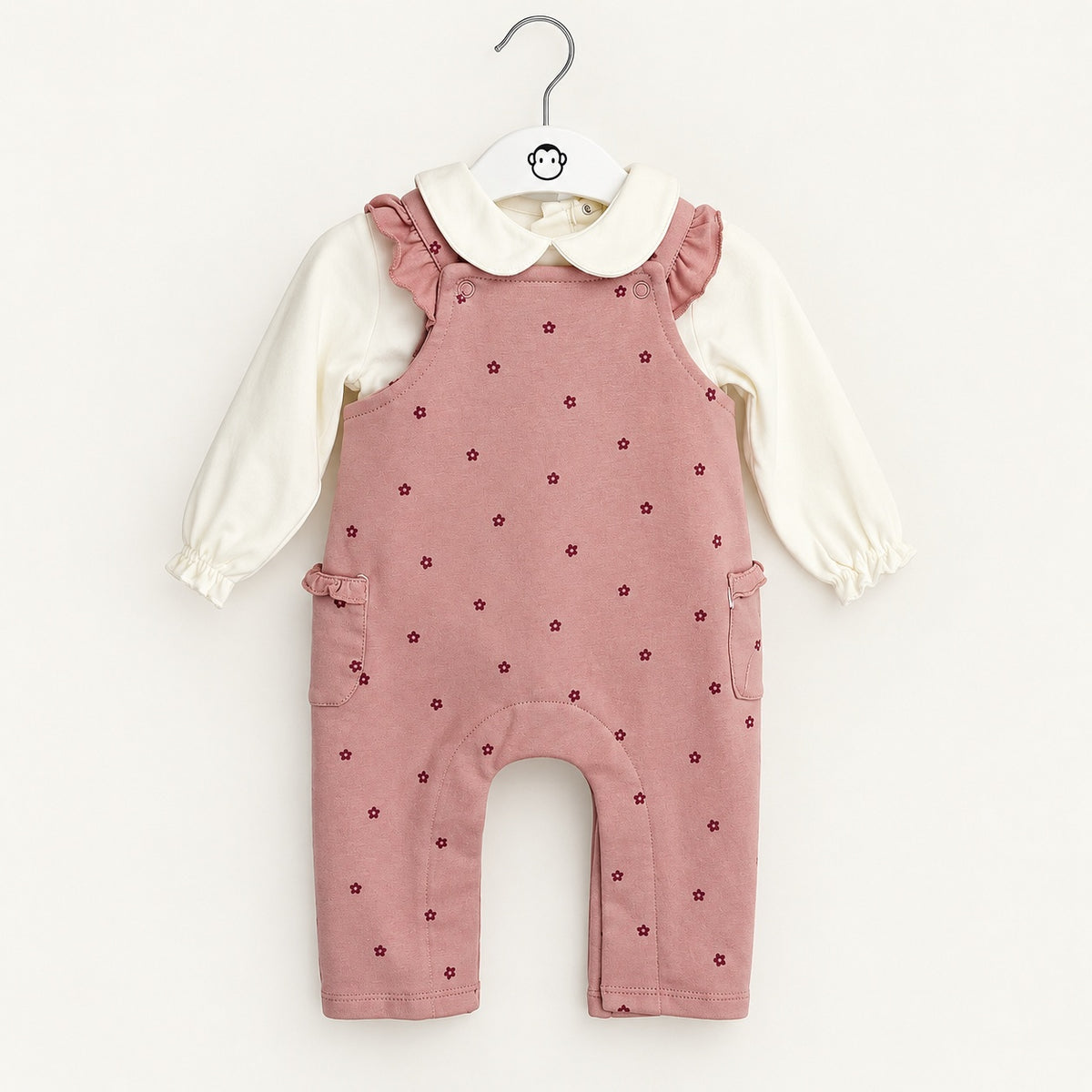 Jardineiras rosa velho com pequenas flores bordô, folhos nas alças e bolsos laterais, combinadas com camisola pérola de manga comprida, gola arredondada e punhos franzidos.
